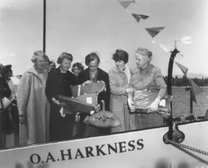 Group of Women with Mrr. Harness (right) Inspecting a Life Jacket on the O.A. Harkness Boat